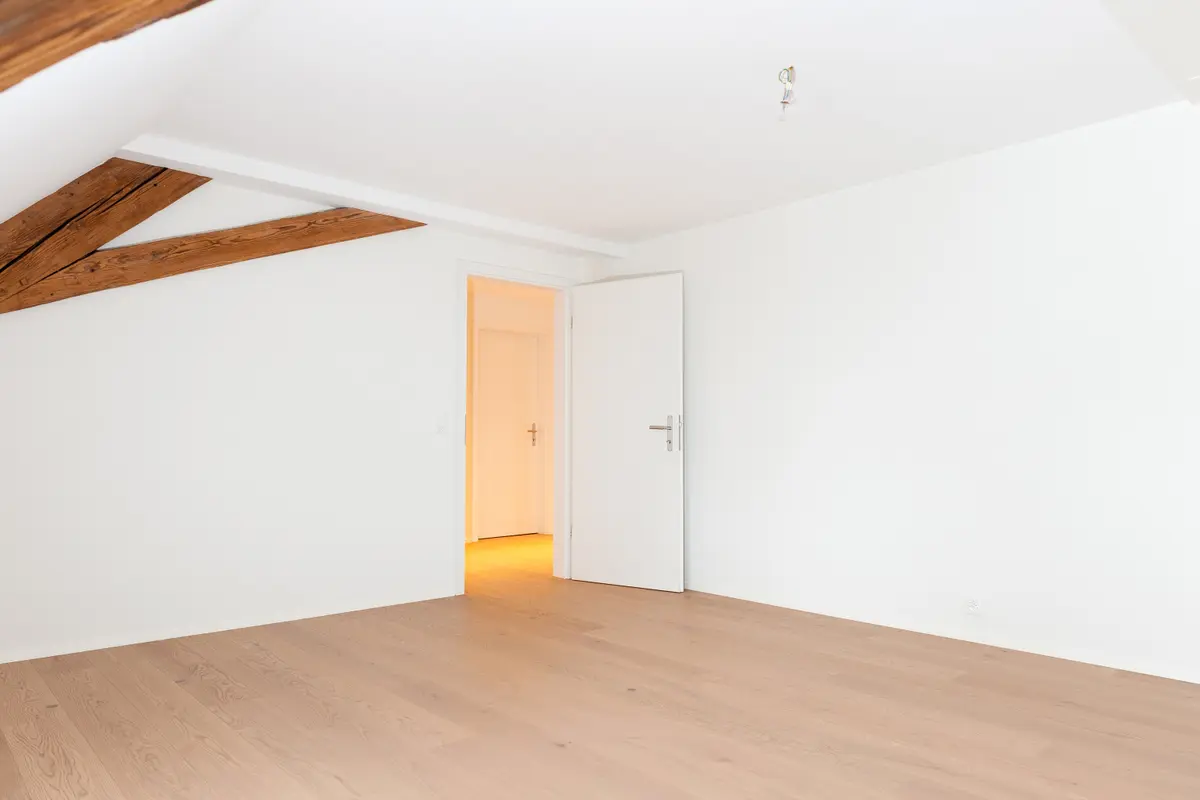 Weiß gestrichenes Zimmer mit Holzboden und offenem Türdurchgang.